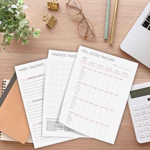 K&ouml;nnte beinhalten: Auf einem Holztisch liegen mehrere gedruckte Tracker, darunter ein Habit Tracker und ein Feel Good Tracker. Die Tracker enthalten Abschnitte f&uuml;r Morgenroutinen, Freundlichkeit und Tagesziele. Weitere Artikel sind ein Laptop, ein Taschenrechner, Stifte und goldene B&uuml;roklammern.
