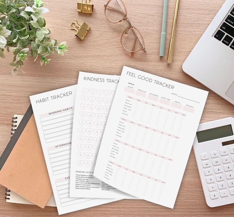 K&ouml;nnte beinhalten: Auf einem Holztisch liegen mehrere gedruckte Tracker, darunter ein Habit Tracker und ein Feel Good Tracker. Die Tracker enthalten Abschnitte f&uuml;r Morgenroutinen, Freundlichkeit und Tagesziele. Weitere Artikel sind ein Laptop, ein Taschenrechner, Stifte und goldene B&uuml;roklammern.