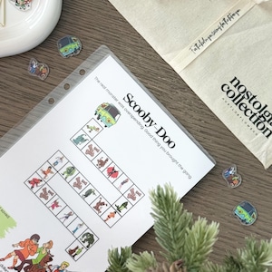 May include: A printed Scooby-Doo board game on white paper, with the text "Scooby-Doo" and "The real monster was overspending. Good thing you brought the gang." A beige tote bag with the text "nostalgia collection" and several pins are also visible.