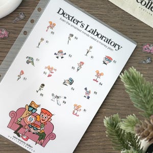 May include: A white sheet with the text "Dexter's Laboratory" and cartoon characters. The sheet is in a clear plastic sleeve. The text "Even the smartest minds need a money plan" is also visible. The sheet is on a wooden surface.