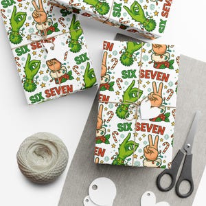 May include: Gift wrap featuring a repeating pattern of green hands, peace signs, and the text "SIX SEVEN" in red. The design includes candy canes, stars, and festive elements. The scene includes wrapped gifts, twine, scissors, and blank tags.