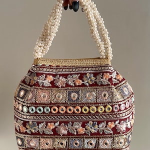 May include: A small, red, embroidered clutch bag with a pearl handle. The bag is decorated with colorful sequins and mirror work.