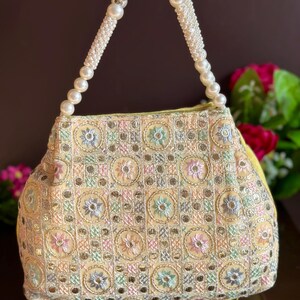 May include: A yellow handbag with a pearl handle. The bag is decorated with a colorful embroidered pattern of flowers and geometric shapes.
