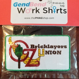 Könnte beinhalten: Ein weißer gestickter Aufnäher mit grünem Rand. Der Aufnäher zeigt eine rote und gelbe Ziegelstraße mit einem grünen Besen und dem Text "Bricklayers Union".