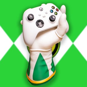 May include: A white Xbox controller with black joysticks and colored buttons is held by a white glove with green and gold accents. The background is a green and white diamond pattern, suggesting a gaming or pop culture theme.