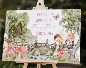 May include: A welcome sign for a first birthday party with a fairy theme. The sign is printed on white cardstock with a watercolor illustration of a whimsical forest scene with fairies, a bridge, and flowers. The text on the sign reads "Welcome to Sophie's Fairy First Birthday". The sign is 36 inches by 24 inches.