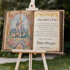 Könnte beinhalten: Ein Holzschild auf einer Staffelei mit einem offenen Buchdesign mit einer Märchenschloss-Illustration und dem Text "Once Upon a Time". Das Schild ist 91 cm x 61 cm groß und enthält den Namen "Baby Morgan".
