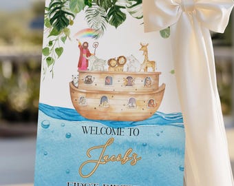 May include: A welcome sign for a first birthday celebration. The sign features an illustration of Noah's Ark with animals, a rainbow, and the text "Welcome to Jacobs First Birthday" in gold script. The sign is displayed on a gold easel.