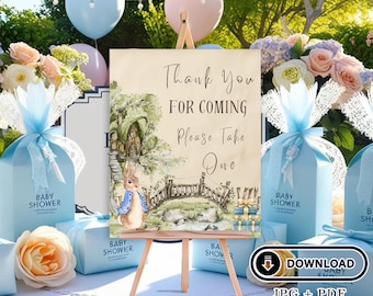 May include: A light brown sign with a watercolor illustration of a rabbit and a bridge. The sign says "Thank You For Coming Please Take One". The sign is on a wooden easel and is surrounded by blue and white gift boxes.