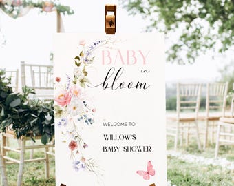 Może przedstawiać: Biały znak z kwiatowym wzorem i tekstem "Baby in Bloom" w kolorze różowym i czarnym. Na znaku widnieje również napis "Witamy na Baby Shower Willow" oraz różowy motyl.
