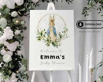 May include: A white sign with a watercolor illustration of Peter Rabbit in a gold circle with green leaves. The sign says "Welcome to Emma's Baby Shower".