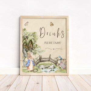 May include: A printable sign with a watercolour illustration of Peter Rabbit and a duckling standing by a bridge. The sign says "Drinks Please Enjoy!" in brown text.