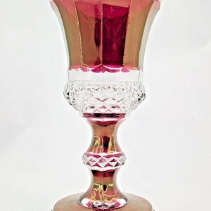 Puede incluir: Un jarrón de cristal alto y ornamentado con una parte superior acampanada y una base ancha y redonda. El jarrón tiene un acabado iridiscente rojo rubí y dorado. La base y la sección media tienen un patrón de corte de diamante. El jarrón mide unos 25 cm de alto.