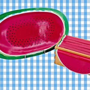 Puede incluir: Una bandeja para servir con temática de sandía y una caja de madera con un diseño de rodaja de sandía. La bandeja es de forma ovalada con un interior rojo, detalles de semillas negras y una corteza verde. La caja tiene una tapa roja y una rodaja de sandía en el lateral.