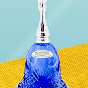 May include: A cobalt blue cologne bottle with a silver pineapple-shaped stopper. The bell-shaped bottle has a diamond-cut pattern and a label that reads "Moonwind Cologne". The bottle contains 3.75 fl oz.