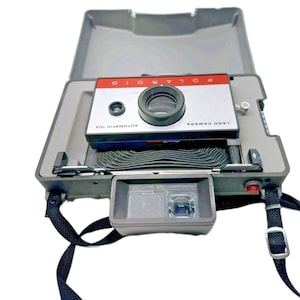 May include: A vintage Polaroid Land Camera 104 in a gray case. The camera has a red and silver face with the word "POLAROID" across the top. The lens is black, and the camera has a black strap.