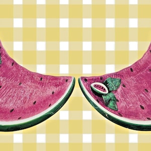 Puede incluir: Dos fuentes de cerámica con forma de sandía. Los platos son rosas con detalles de semillas negras y una corteza verde. Cada plato tiene una pequeña rodaja de sandía decorativa y hojas verdes. El fondo es un patrón de cuadros amarillos y blancos.