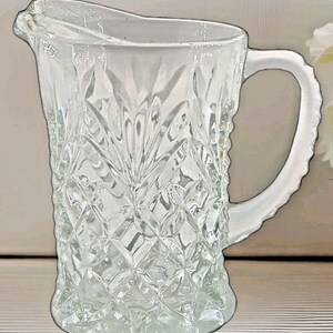 Könnte beinhalten: Ein klarer Glaskrug mit einem Diamant- und Blättermuster. Der Krug hat einen Griff und einen Ausguss zum Ausgießen. Der Krug wird wahrscheinlich zum Servieren von Getränken verwendet.
