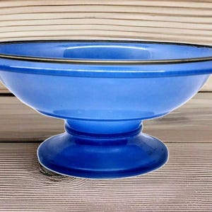 May include: A vibrant blue pedestal bowl with a wide, shallow design. The bowl features a contrasting dark rim and a rounded base. This decorative piece is suitable for serving or display.