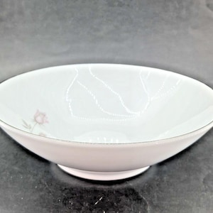 Könnte beinhalten: Weißes Porzellan-Servierschüssel mit zartem rosa Blumendesign und silbernem Rand. Die Schüssel hat eine flache, ovale Form und einen kleinen, runden Sockel. Ein dezentes Punktmuster verziert das Innere. Ideal zum Servieren von Salaten oder Beilagen.