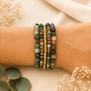 May include: A set of five stacked beaded bracelets featuring a variety of round gemstone beads in shades of forest green, sage, and muted mauve, interspersed with small metallic copper-toned spacer beads and a central strand of gold-toned beads.