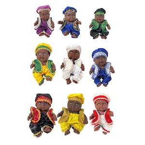 May include: Nine small dolls with dark skin and various colorful outfits are arranged on a white background. The dolls wear hats and matching outfits in colors like purple, blue, green, yellow, white, and red. Each doll has a unique facial expression.