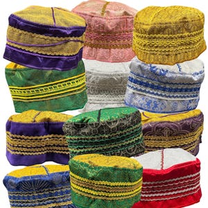 May include: A collection of colorful, patterned kufi hats. The hats feature various colors, including gold, purple, green, and blue, with decorative trim and embroidery. The hats are stacked, showcasing the variety of designs and colors.