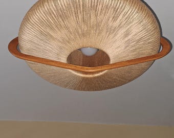 May include: A mid-century modern pendant light fixture. The light has a circular shape with a woven beige shade and a wooden ring around the center. The fixture is suspended from a brown wooden canopy.