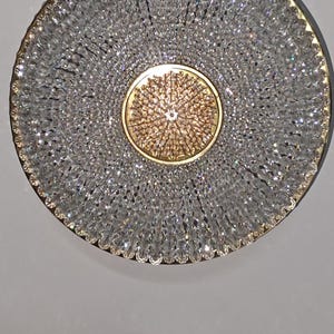 May include: A round, gold-toned ceiling light fixture with a central, circular, gold-toned design surrounded by clear crystal beads.