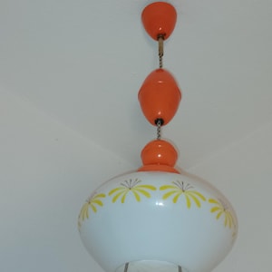 Könnte beinhalten: Eine weiße Deckenleuchte mit gelbem Blumendesign und drei orangefarbenen Hängekugeln.