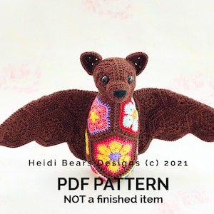 May include: A crocheted bat with brown wings and body, and a colorful floral design on its chest. The bat has small ears and a detailed face. The image includes the text "Heidi Bears Designs (c) 2021" and "PDF PATTERN NOT a finished item."