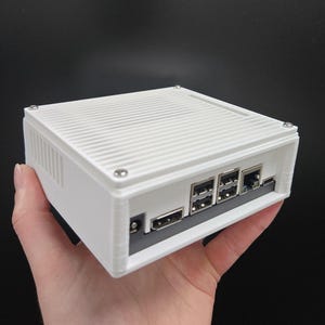 May include: A white rectangular electronic device with a ridged top and multiple ports. The device is held in a hand against a black background. The ports include USB and Ethernet connections.