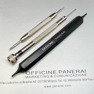 May include: Three watch repair tools. Two are silver with textured handles and pointed tips. The third is black with "OFFICINE PANERAI" printed on it. The tools are on a white surface with printed text.