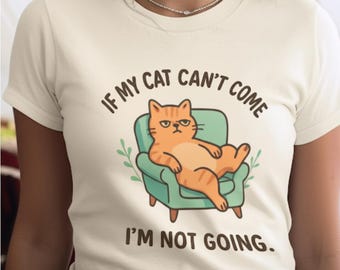 May include: Cream-colored t-shirt featuring a cartoon cat lounging in a teal armchair. The orange cat has a grumpy expression. Text on the shirt reads, "IF MY CAT CAN'T COME I'M NOT GOING."