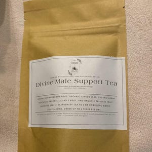 May include: A brown paper bag with a white label featuring the text "Divine Male Support Tea." The label lists ingredients like organic ashwagandha root and suggests steeping the tea for 10 minutes. The bag is sealed at the top.
