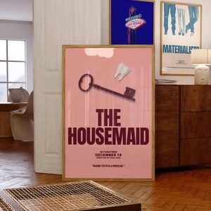 May include: A framed movie poster for "The Housemaid" with a pink background, a key, and a tooth graphic. The poster includes the text "In Theatres December 19" and "Having Teeth Is A Privilege."