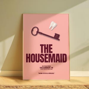 May include: A framed poster with a pink background. It features a key and a tooth graphic. The title "THE HOUSEMAID" is in large maroon letters. Additional text includes "IN THEATRES DECEMBER 19" and a quote: "HAVING TEETH IS A PRIVILEGE."