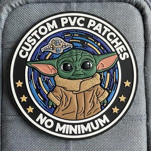 May include: A circular, black PVC patch with a green alien character wearing a brown coat. The patch has the text "CUSTOM PVC PATCHES" and "NO MINIMUM" in white, with gold stars. A spaceship is also featured in the design.