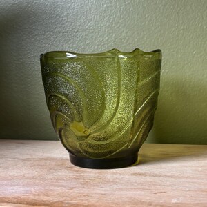 Peut inclure: Un bol en verre vert olive translucide présentant une surface texturée avec un motif en spirale tourbillonnant qui rayonne depuis le centre. Le bord du bol a un contour festonné et la base est lisse et circulaire, offrant une assise stable.