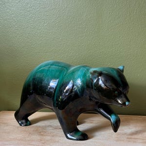 Könnte beinhalten: Eine Keramikbärenfigur in schreitender Pose mit einer glänzenden Glasur, die von einem tiefen, dunklen Schwarz an der Basis zu einem lebendigen, satten Smaragdgrün über den Rücken und die Schultern übergeht, mit glatten Konturen und Ohren.
