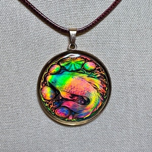 May include: A round pendant necklace featuring a colorful koi fish design. The pendant has a gold-colored frame and a rainbow-colored fish. The necklace has a dark red cord.