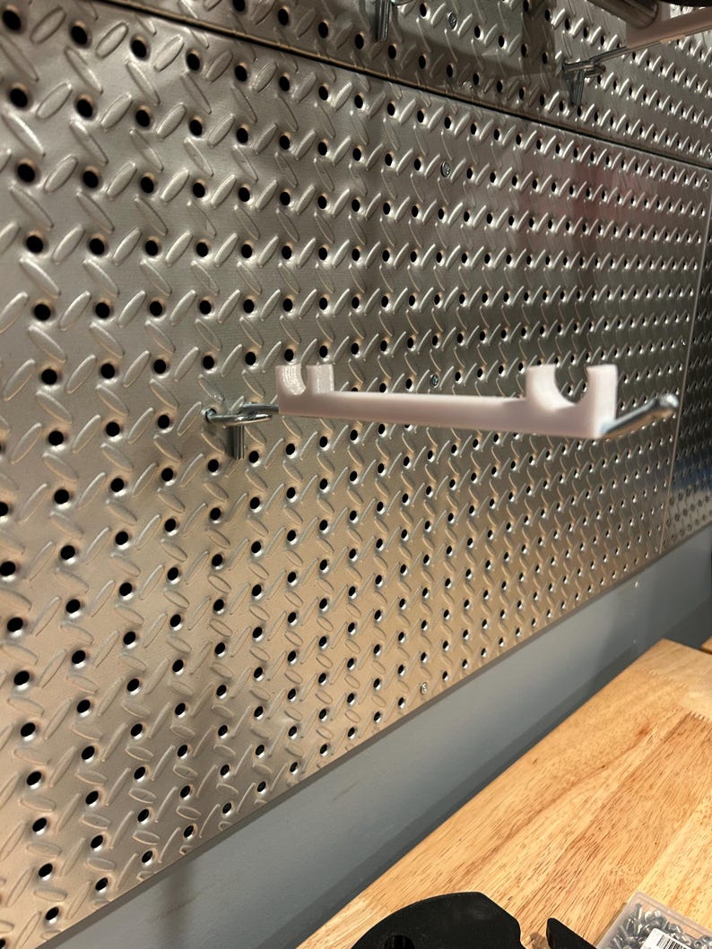 May include: A white metal shelf bracket mounted on a silver pegboard wall.