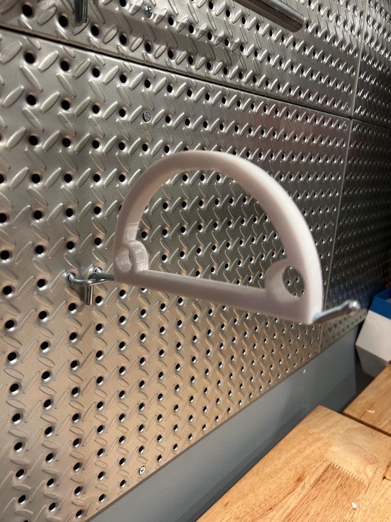 May include: White plastic pegboard hook with a curved design. The hook is mounted on a silver pegboard.