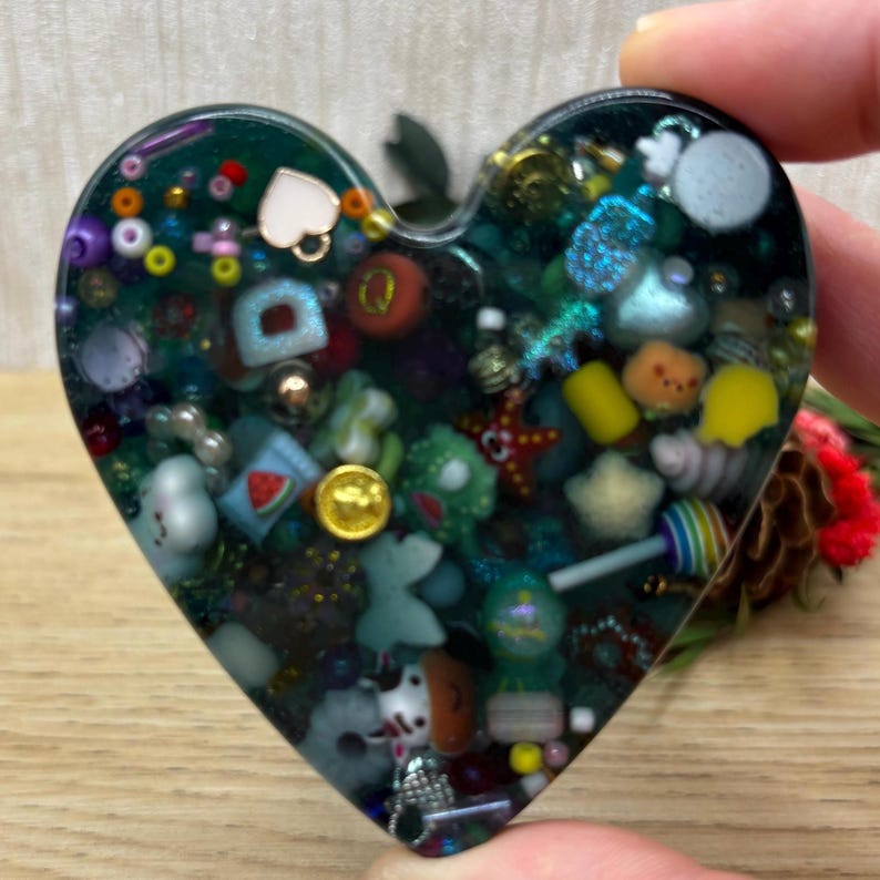 A mini heart shaped picky pad. The colour is blue. It is made from a reusable material and includes beads, charms, flatbacks and other embellishments.