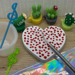 Op de afbeelding: Een verzameling miniatuur decoratieve items, waaronder een hartvormig object met rode stippen, een tandheelkundig instrument en kleine cactus- en konijnenbeeldjes in bekers. Er zijn ook muzieknootvormige roerstaafjes en een doorzichtige container.