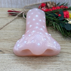Op de afbeelding: Een lichtroze glazen object met witte stippen. Het object heeft een belvorm met een uitlopende basis en een afgeronde bovenkant. De basis heeft drie gebogen openingen. Decoratie-artikel.