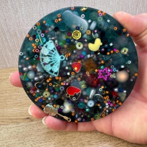 A circle shaped picky pad. The colour is blue. It is made from a reusable material and includes beads, charms, flatbacks and other embellishments.
