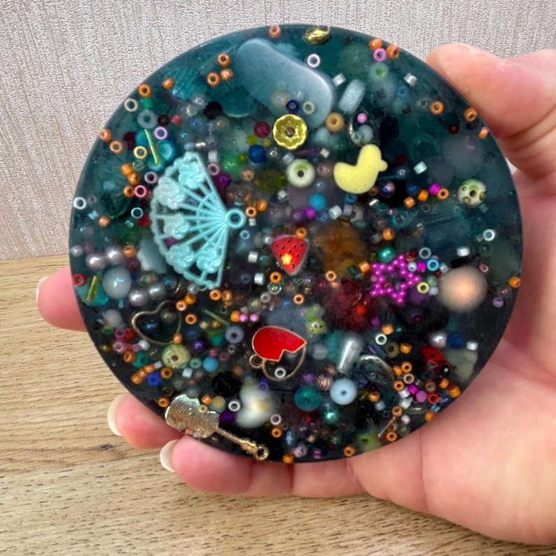 A circle shaped picky pad. The colour is blue. It is made from a reusable material and includes beads, charms, flatbacks and other embellishments.