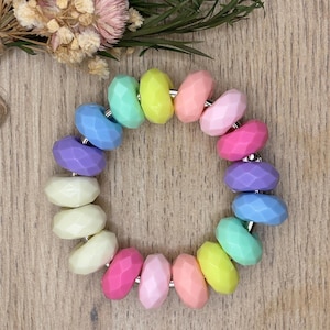 May include: A colorful bracelet featuring faceted beads in a variety of pastel colors, including pink, blue, yellow, green, and purple. The beads are strung together with silver-colored metal connectors, creating a vibrant and playful accessory.