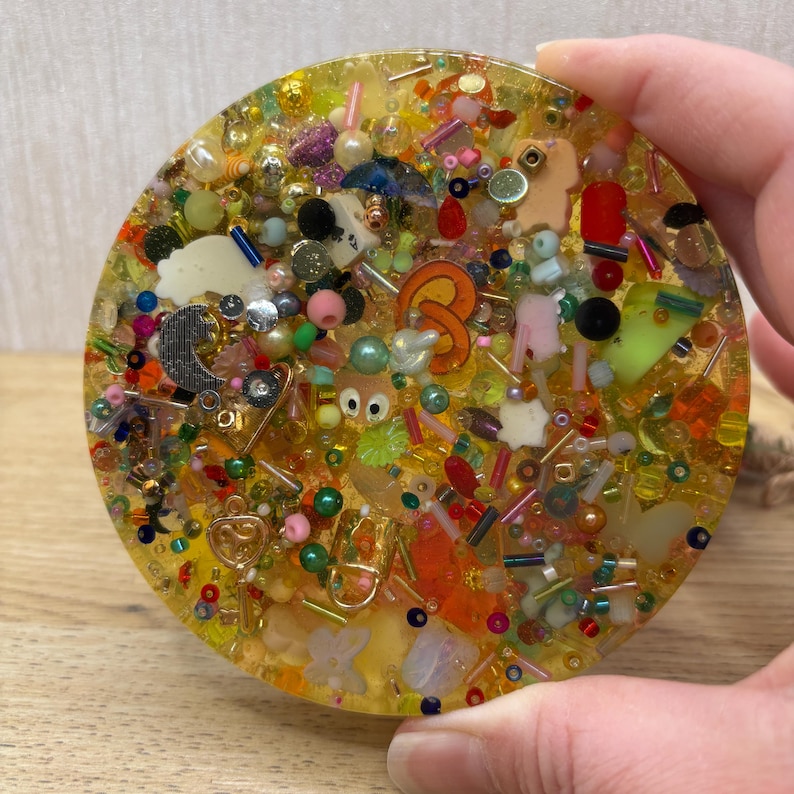A yellow coloured picky pad in a circle shape. The sensory toy contains a variety of beads, charms, and other embellishments.